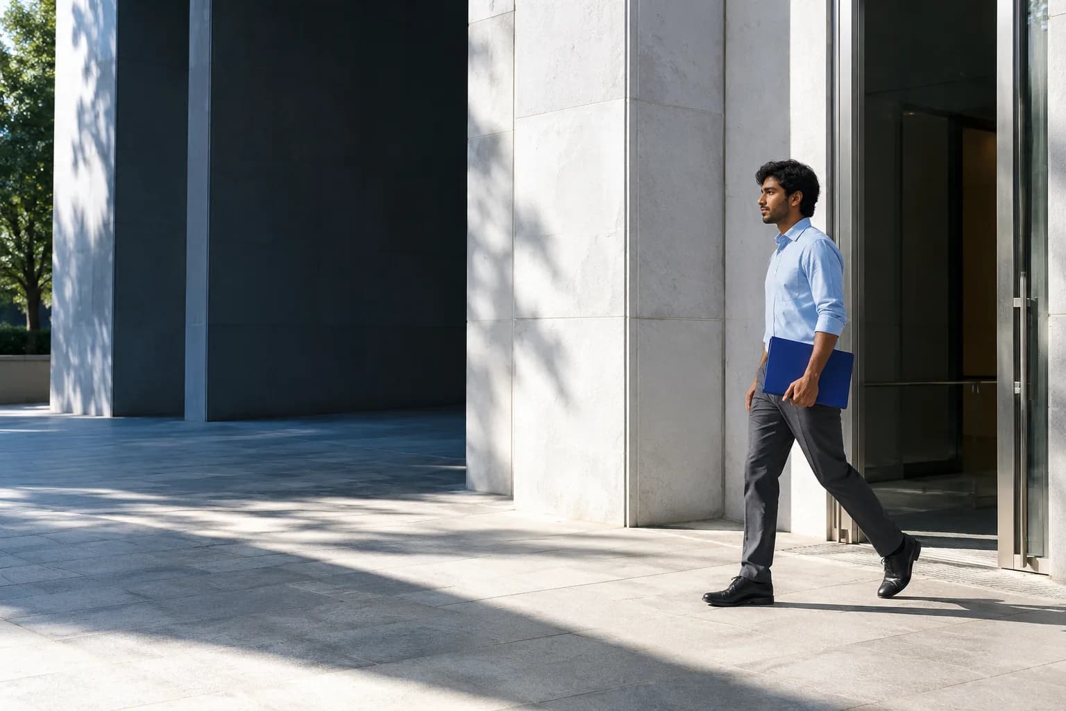 A professional carrying a blue folio through a sunlit building entrance